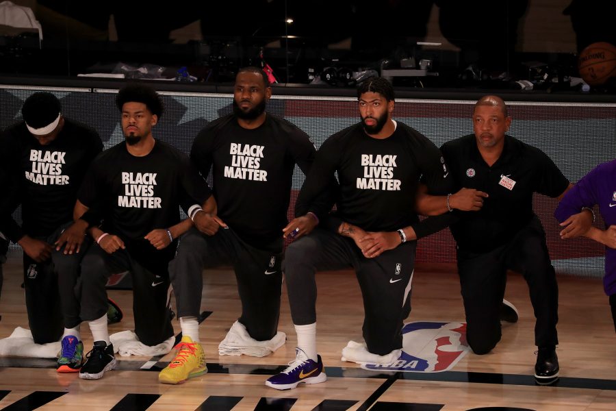 The Los Angeles Lakers, including LeBron James and Anthony Davis, wear Black Lives Matter shirts while kneeling during the national anthem prior to a game against the Los Angeles Clippers and head coach Doc Rivers, right, at The Arena at ESPN Wide World Of Sports Complex in Lake Buena Vista, Florida, on Friday, July 30, 2020. Photo courtesy of Mike Ehrmann/Getty Images/TNS