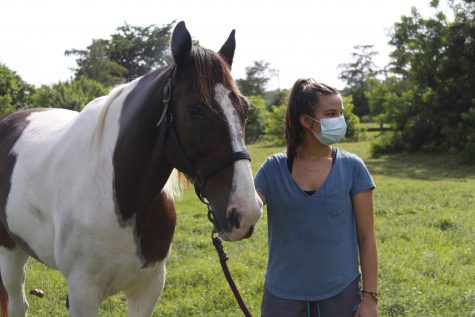 Female student wearing a mask next to a horse she rides as an extracurricular activity.