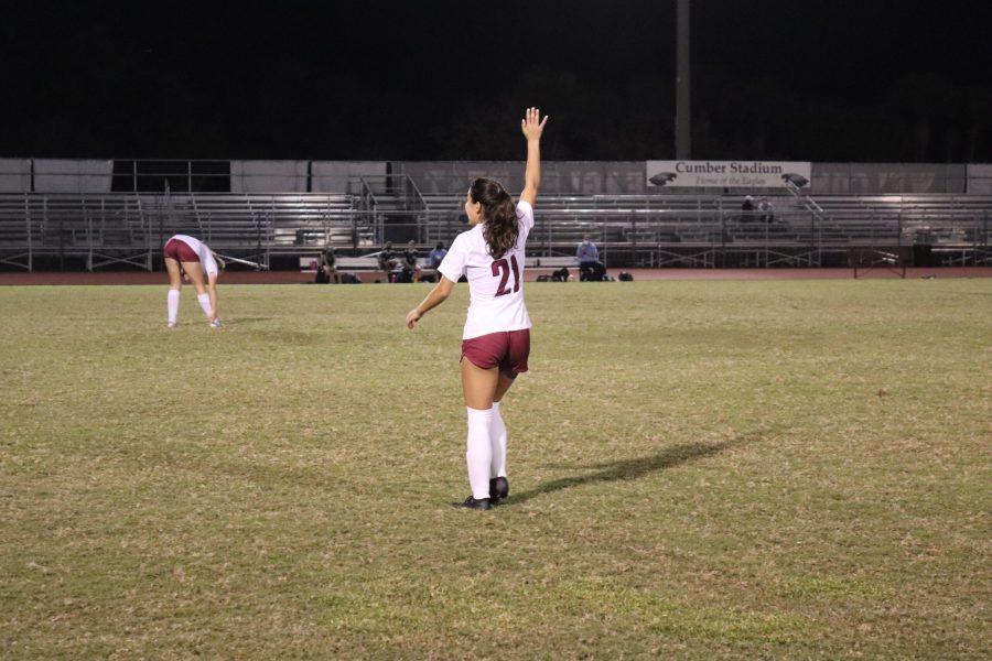 Standing in the middle of the field, forward Victoria Alvarez (21) puts her right hand in the air to call out to her teammates.