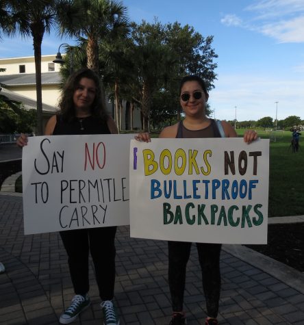 Candidate for U.S. Congress Hava Holzhauer and a fellow protestor hold up signs advocating for gun control. Their signs read Say NO to permitless carry and Books Not Bulletproof Backpacks. 