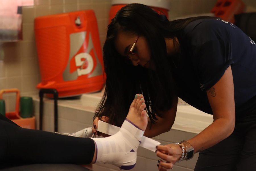 Nitfrancis Marrero works diligently to tape an athletes ankle before their upcoming game. This provides stability, support, and compression for the ankle joint.