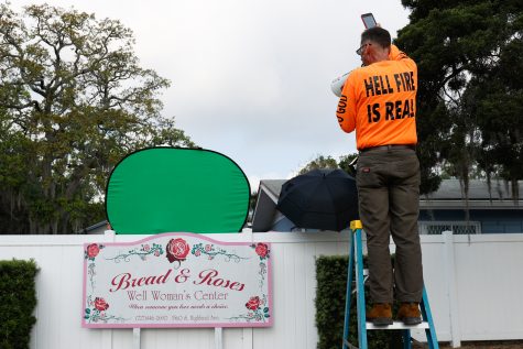 Victor McCleskey of New Port Richey, left, uses a ladder to look over a privacy fence outside of Bread and Roses Womans Health Center in Clearwater on Saturday. Less than 48 hours earlier, Florida Gov. Ron DeSantis signed a bill to ban abortion at six weeks. Photo permission from Jefferee Woo/TNS.