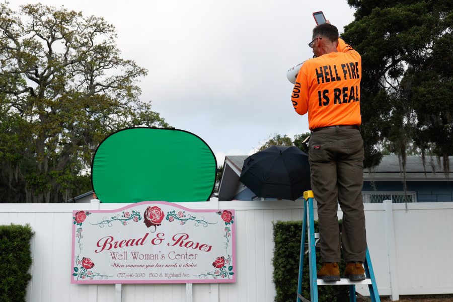 Victor McCleskey of New Port Richey, left, uses a ladder to look over a privacy fence outside of Bread and Roses Woman's Health Center in Clearwater on Saturday. Less than 48 hours earlier, Florida Gov. Ron DeSantis signed a bill to ban abortion at six weeks. Photo permission from Jefferee Woo/TNS.