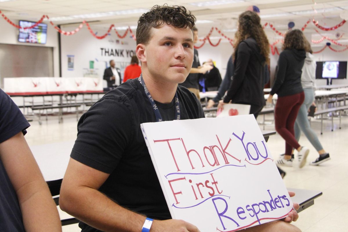 Feeding First Responders. Senior Ethan Askin holds a greeting sign at the First Responders Breakfast in the cafeteria. Askin and the other volunteers for the project made signs, prepared gift bags and served food for the first responder attendees.