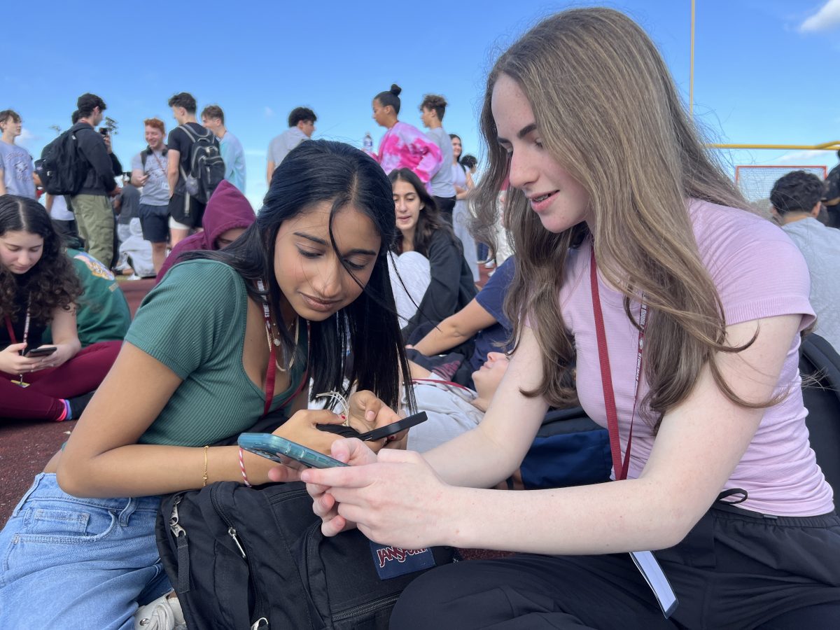 Patiently waiting to be permitted back into school, junior Aesha Bhavsar and sophomore Sarah Rosaler prepare for their upcoming Florida Forensics League Varsity States by reviewing notes on their cell phone. MSD students were instructed to evacuate to Cumber Stadium following a bomb threat during fifth period on Wednesday, Feb. 28. “I am frustrated that I am losing my study hall class time to work on my debate speech,” Rosaler said.
