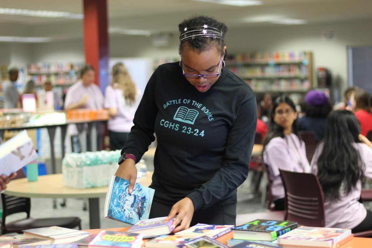 Junior Christina Paillant from Coral Glades High School examines the  variety of novels displayed at Marjory Stoneman Douglas High Schools media center after the Battle of the Books competition on April 17. The event united book club members from across Broward County to compete against each other using their knowledge on the selected books.