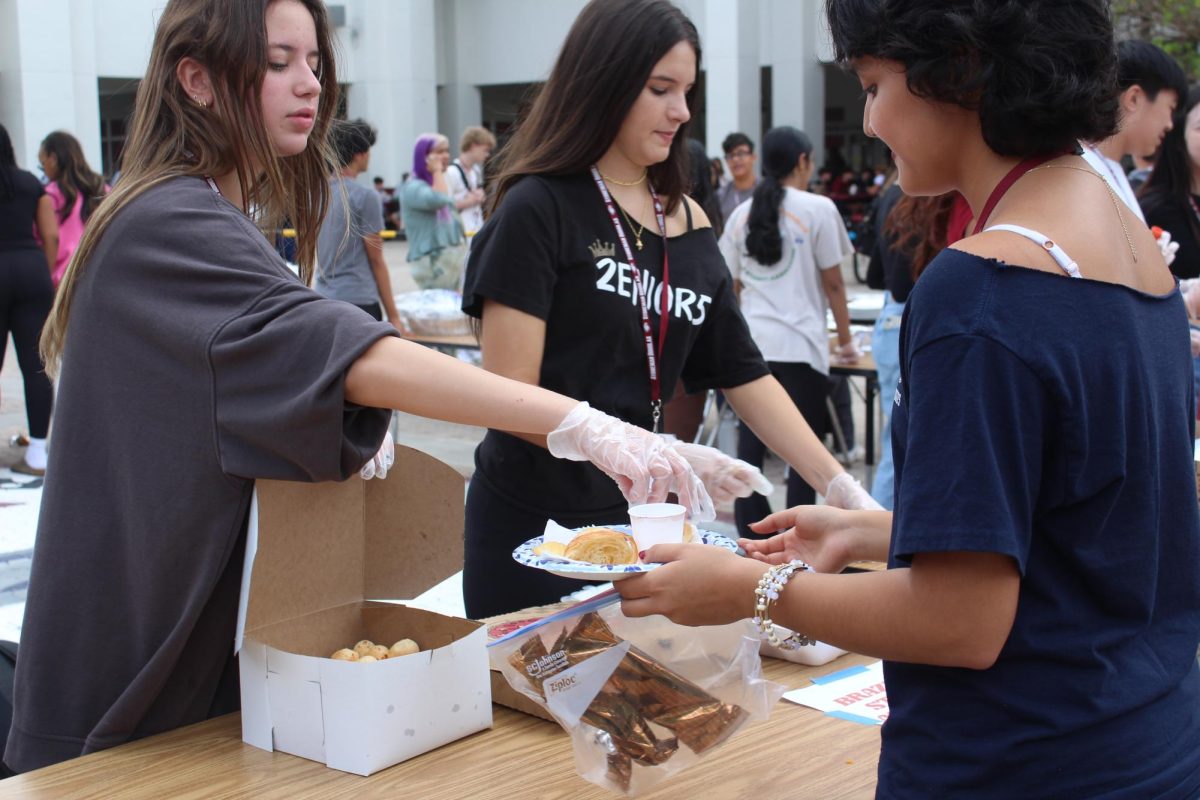 Seniors Amanda Pugatch and Melissa Azzarito serve sophomore Victoria Figueroa pao de queijo at the Cultural Food Fair hosted by the Indian Student Association on Oct. 30. The Brazilian Student Association and many other cultural clubs participated in the fair, which students could enjoy for $5 during both A and B lunches. "The food fair is a very nice way for cultures to blend and for people to diversify their existing palettes," Figueroa said.