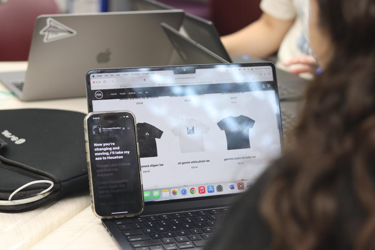 Senior Lyla Sachs listens to the new Role Model deluxe album, "Kansas Anymore (The Longest Goodbye)," as she scrolls through his website looking at clothes and merchandise. Role Model released his sophomore deluxe album on Feb. 14, showcasing his musical range.