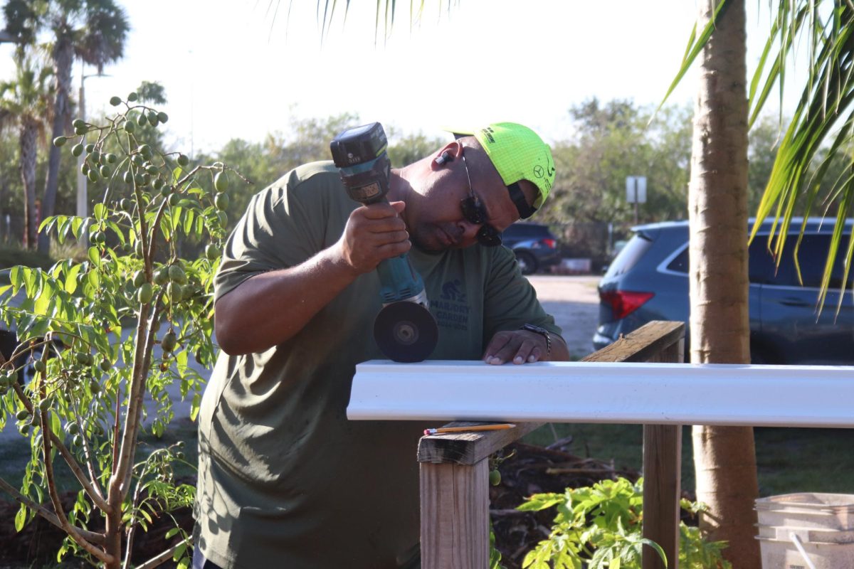 Chemistry teacher Sean Simpson cuts a metal pipe out in the sun. During the Day of Service and Love, Simpson worked on repairing his hydroponics system in Marjory's Garden with the help of a few volunteer students.