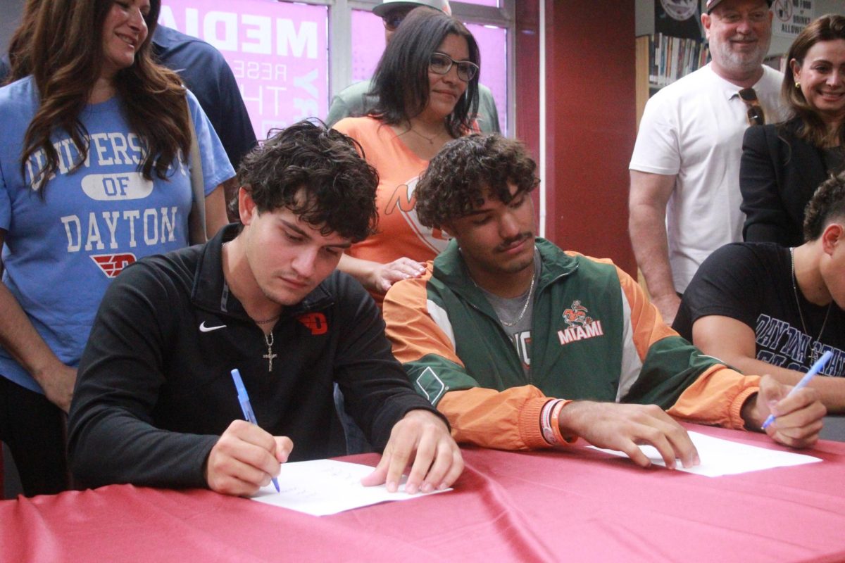 It's Official. Seniors Jake Rizzo (left) and Gio Rojas (right) commit to the University of Daytona and the University of Miami, respectively, to play baseball. On Wed., Nov. 12, in the library, nine student-athletes participated in the annual college signing ceremony. "I think the most challenging thing playing at the college level is the consistency and just the atmosphere with the pressure of the shoes you have to fill in," Rojas said.